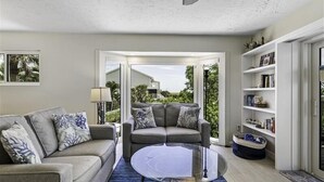 A living room with a grey sofa, a round glass coffee table, and a bookshelf.