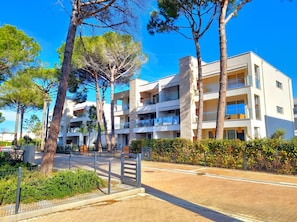 Un hôtel à plusieurs étages, doté de balcons, entouré d’arbres et bordé d’une allée pavée.