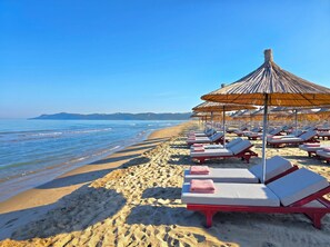 A beach with sun loungers and thatched umbrellas. - SanPietro Holiday Homes 296 (Gjiri Lalzit)