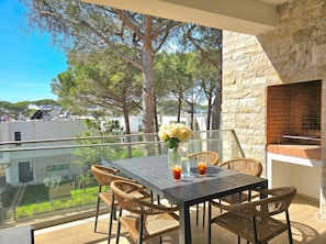 Un balcon avec une table, des chaises, un vase de fleurs et un four en briques.