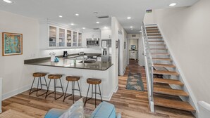 Une cuisine moderne dotée d’un îlot central, de tabourets de bar et d’un escalier en bois.
