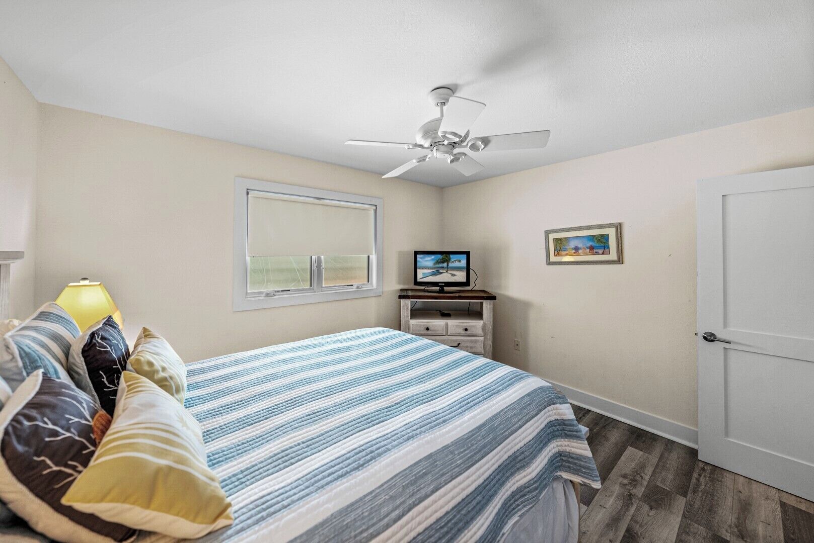 Une chambre à coucher avec un lit, un ventilateur de plafond, une télévision, une fenêtre et une porte.