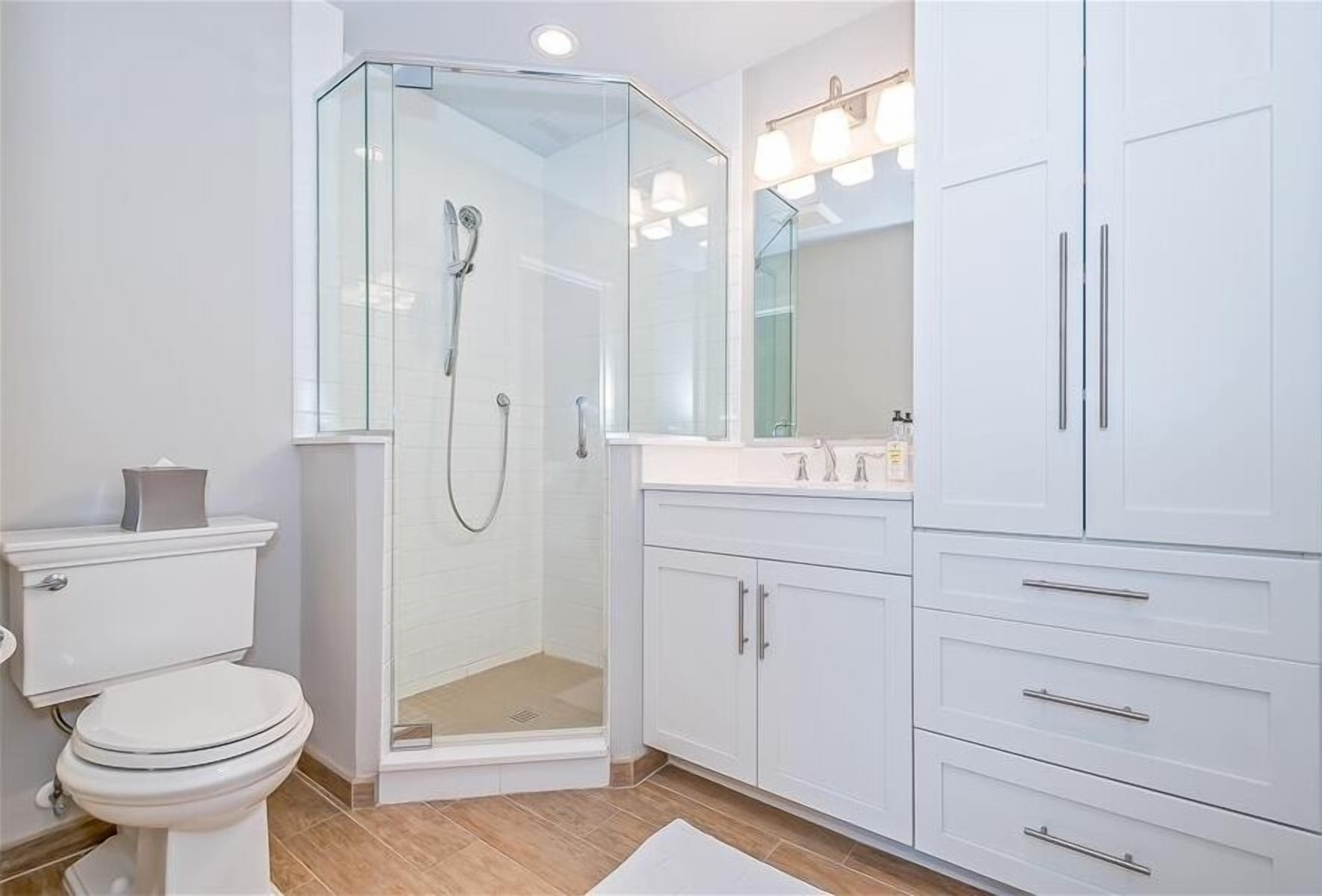 Un baño moderno con cabina de ducha de vidrio, muebles blancos y un inodoro.