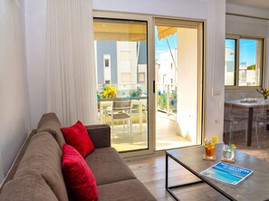 A modern living room with a sofa, a coffee table with a magazine, and a sliding glass door leading to an outdoor dining area.