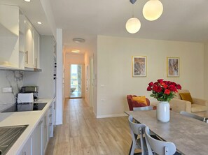 Una cocina moderna con armarios blancos, un comedor con mesa y sillas, y una sala de estar con sofá y un jarrón de rosas rojas.
