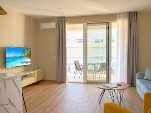 Ein modernes Wohnzimmer mit einem Flachbildfernseher, einer Couch, einem Couchtisch und einem Balkon mit Sitzgelegenheit.