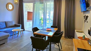 A modern living room with a sofa, dining table, chairs, and a TV. - Wide Beach Apartments 289 (Gjiri Lalzit)