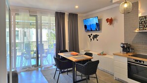 A modern kitchen with a dining area, a TV mounted on the wall, and a view of the outdoors through large windows. - Wide Beach Apartments 289 (Gjiri Lalzit)