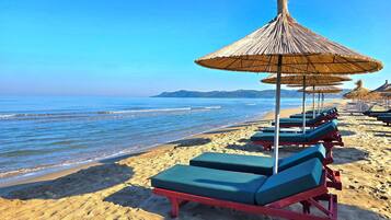 A beach with rows of sun loungers and thatched umbrellas.