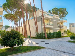 Un immeuble résidentiel moderne à plusieurs étages, doté de balcons et entouré de verdure et d’arbres.