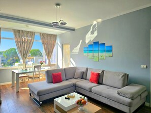 Uma sala de estar moderna com um sofá seccional, uma área de jantar com mesa e cadeiras, e uma janela grande com cortinas.