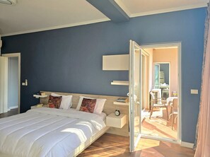 Quarto com cama, mesas de cabeceira, um espelho e porta aberta para uma varanda.