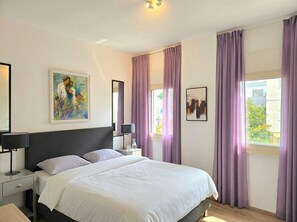 Une chambre à coucher avec un lit, des tables de chevet, une lampe et des œuvres d’art accrochées aux murs.