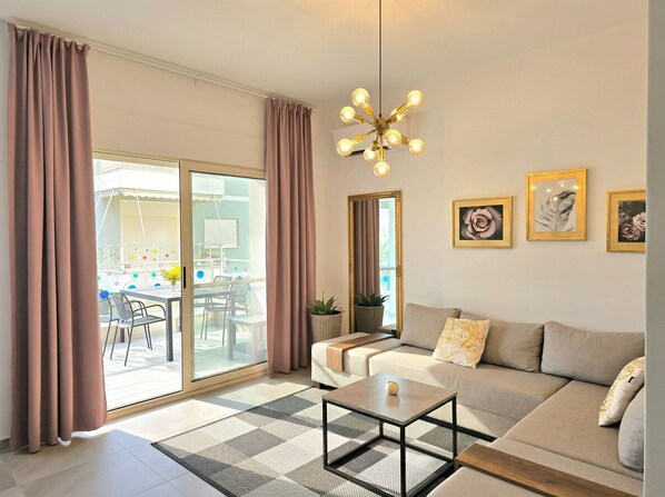 Ein modernes Wohnzimmer mit einer Couch, einem Couchtisch und einer Chandelier. Eine Schiebetür aus Glas führt zu einem Außenbereich mit Tisch und Stühlen.
