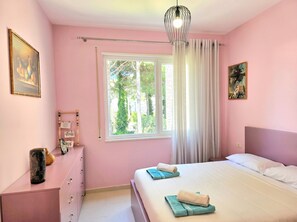 Une chambre à coucher décorée dans des tons de rose, avec un lit, deux oreillers, une table de chevet avec une lampe, une fenêtre avec des rideaux et un tableau accroché au mur.