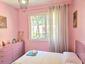 A pink-themed bedroom with a bed, a dresser, a window with curtains, and a painting on the wall.