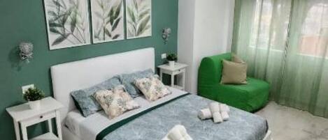 A bedroom with a bed, a nightstand, a green chair, and artwork on the wall.
