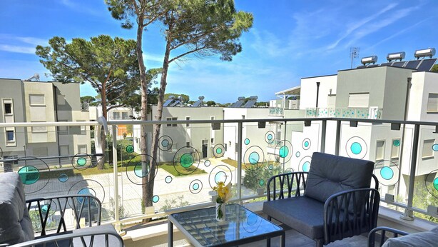 Un balcone con posti a sedere all'aperto, un tavolo in vetro e vista su edifici e alberi.