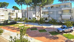 Un complesso residenziale moderno con diversi balconi, un'area di parcheggio e un giardino curato con alberi.