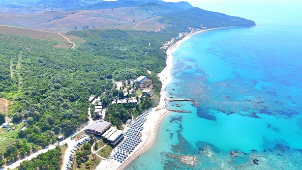 Luftaufnahme einer Küstenlandschaft mit Strand, einer Marina und einem Resort mit mehreren Gebäuden und einem Parkplatz.