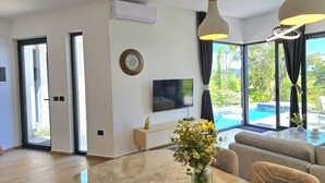 Ein modernes Wohnzimmer mit Esstisch, Sofa und Wandfernseher.