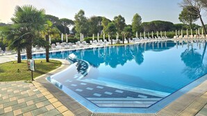 Une piscine entourée d’arbres et de verdure, avec des chaises longues et des parasols.