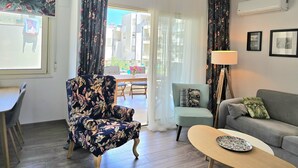 Un salon comprenant un fauteuil à motifs floraux, un canapé, une table basse et un coin repas avec une table et des chaises.