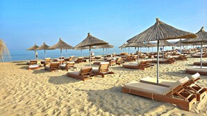 Une plage avec des chaises longues en bois et des parasols en chaume.