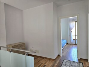 Une pièce avec un plancher en bois, un lit recouvert d’une couverture bleue, une armoire blanche et une porte donnant sur une autre pièce.