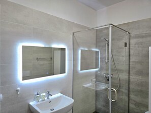 Une salle de bain moderne avec une douche à parois de verre, un lavabo blanc avec un miroir au-dessus, et un luminaire fixé au mur.