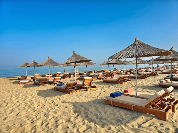 A beach with sun loungers and thatched umbrellas.