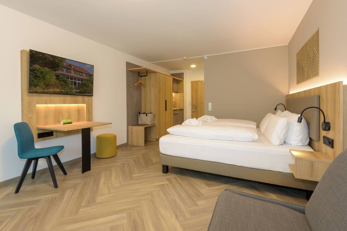 Ein modernes Hotelzimmer mit Bett, Schreibtisch, Stuhl und einem kleinen Hocker.
