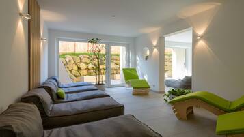 A spa room with a row of massage tables, a green chair, and a stone wall.