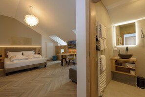 Ein modernes Hotelzimmer mit einem großen Bett, einem Essbereich und einem Badezimmer mit großem Spiegel und Waschbecken.