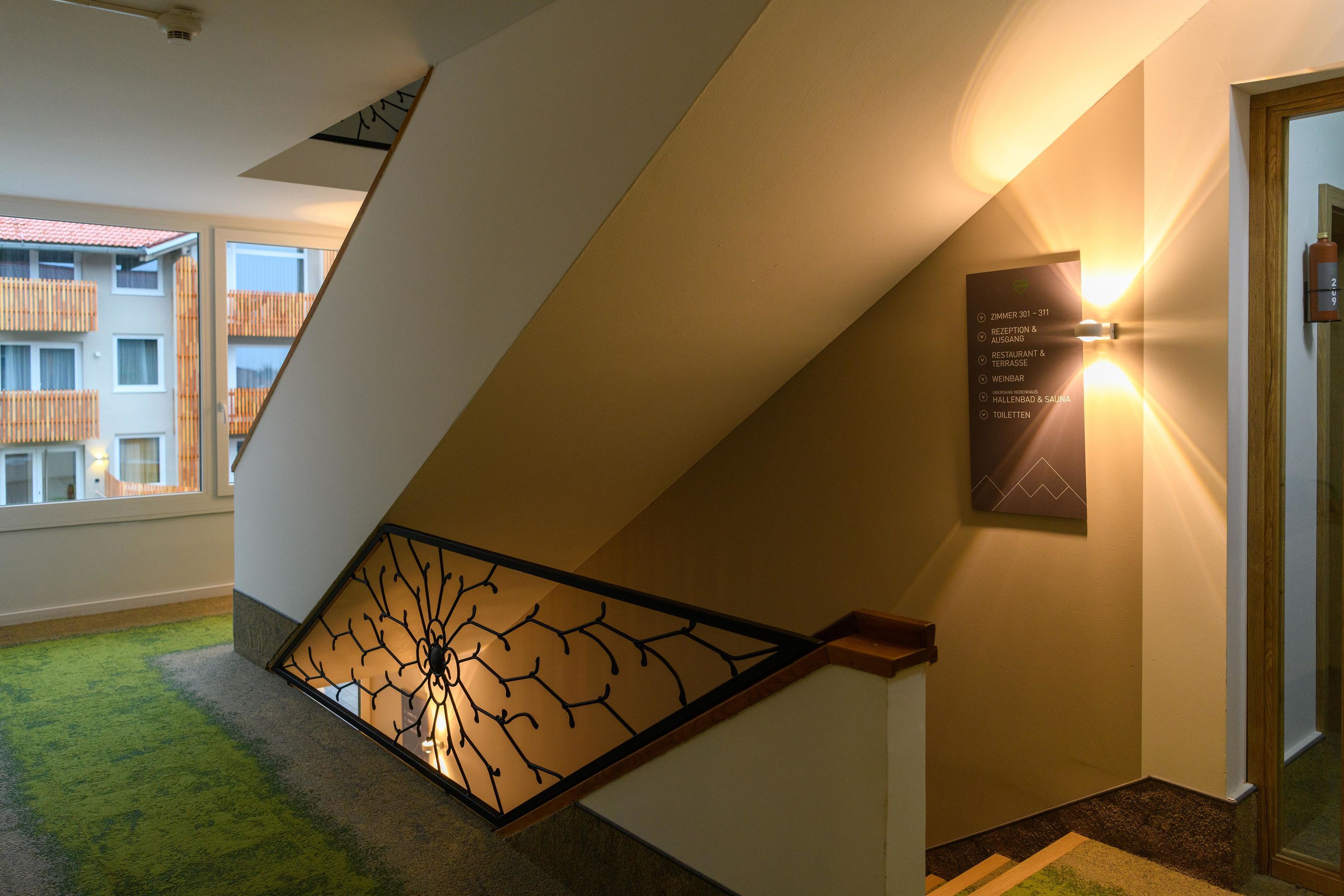 A staircase with a glass railing, a wall-mounted sign with room numbers, and a view of a building with balconies.