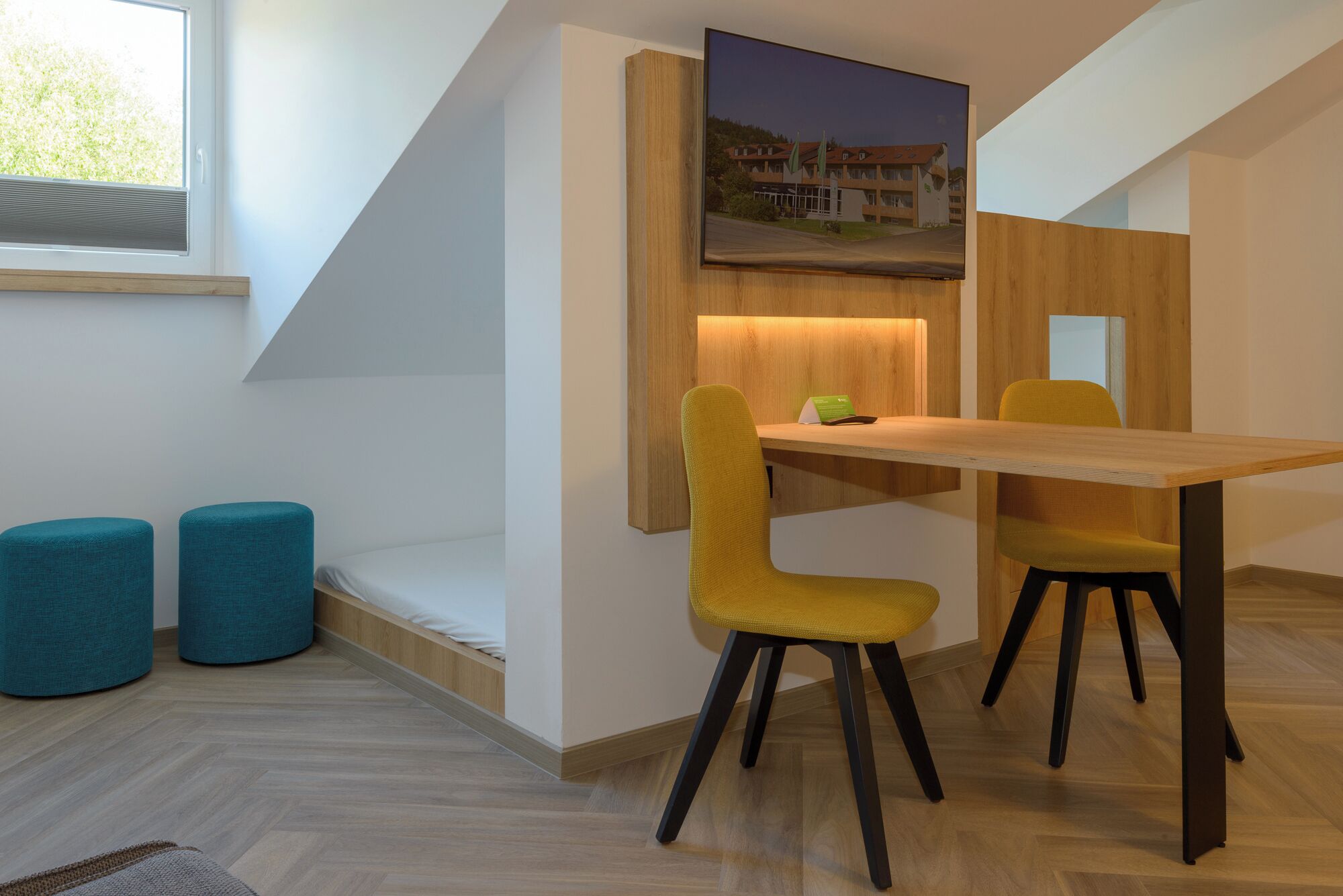 A modern room with a wooden dining table, two yellow chairs, and a teal sofa.