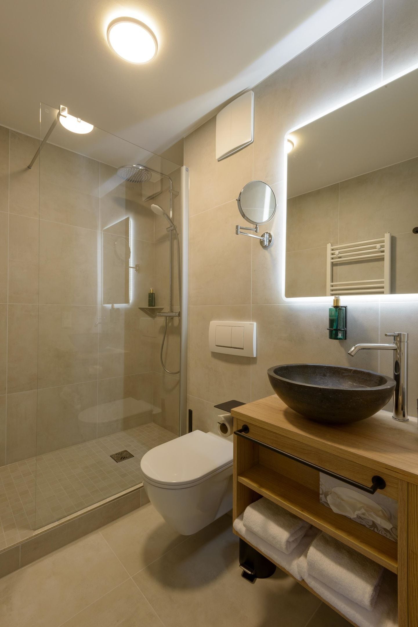 A modern bathroom with a glass-enclosed shower, a white toilet, a wooden vanity with a large bowl sink, and a mirror.