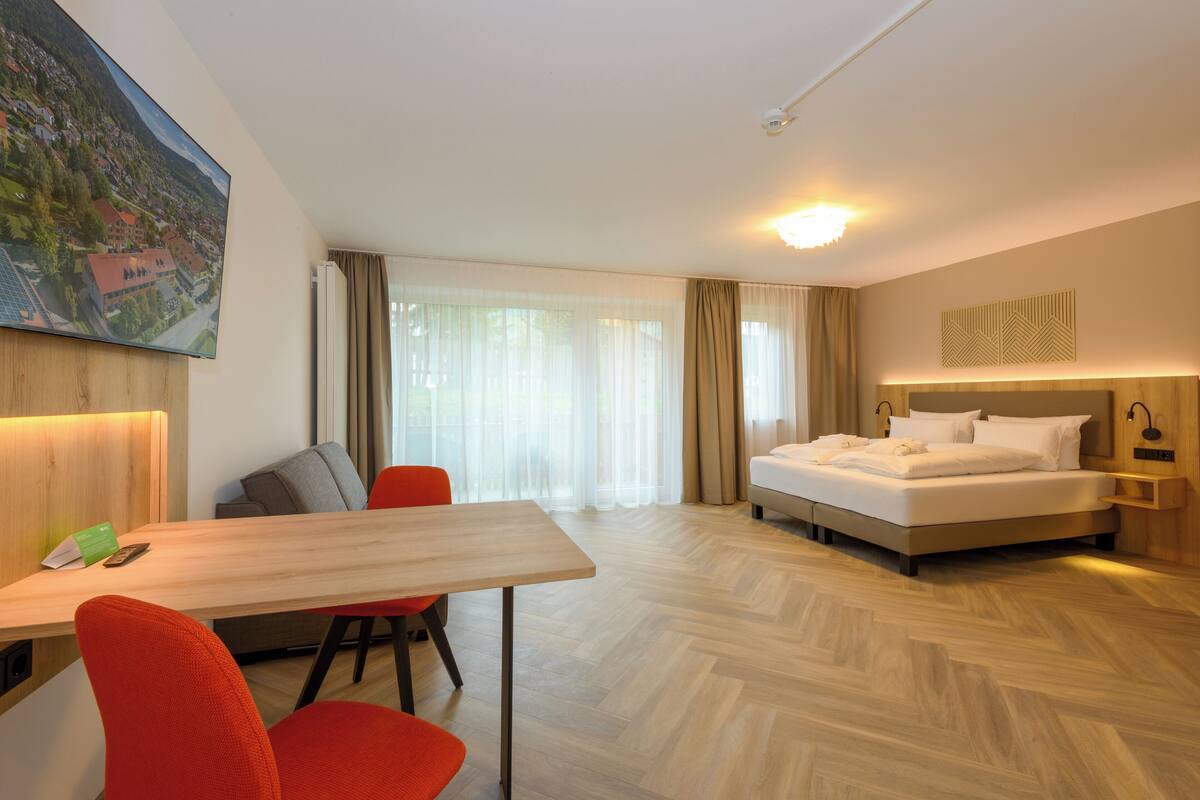 Ein Hotelzimmer mit Bett, Schreibtisch, Stuhl und einem großen Fenster mit Vorhängen.