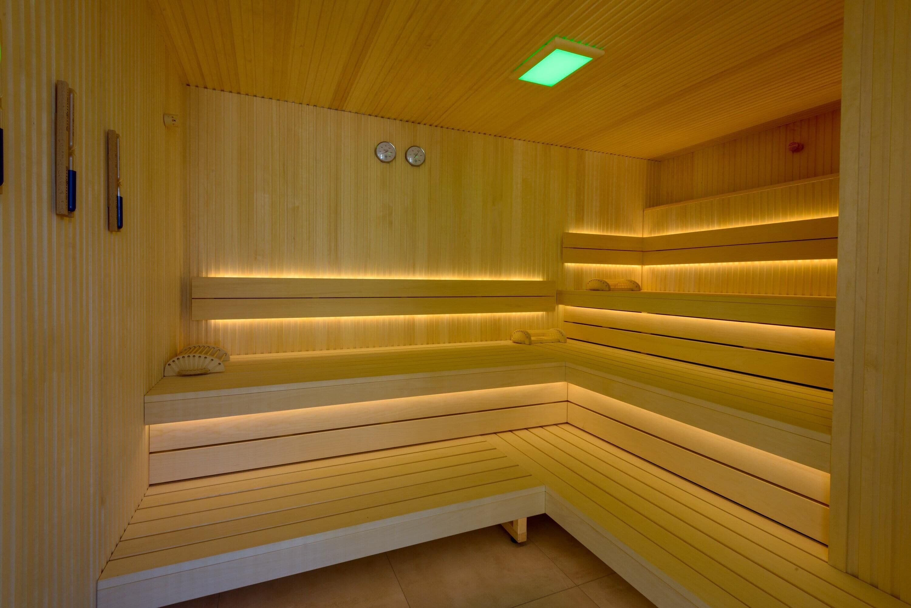 Una sauna con listones de madera, bancos y una luz de techo iluminada en verde.