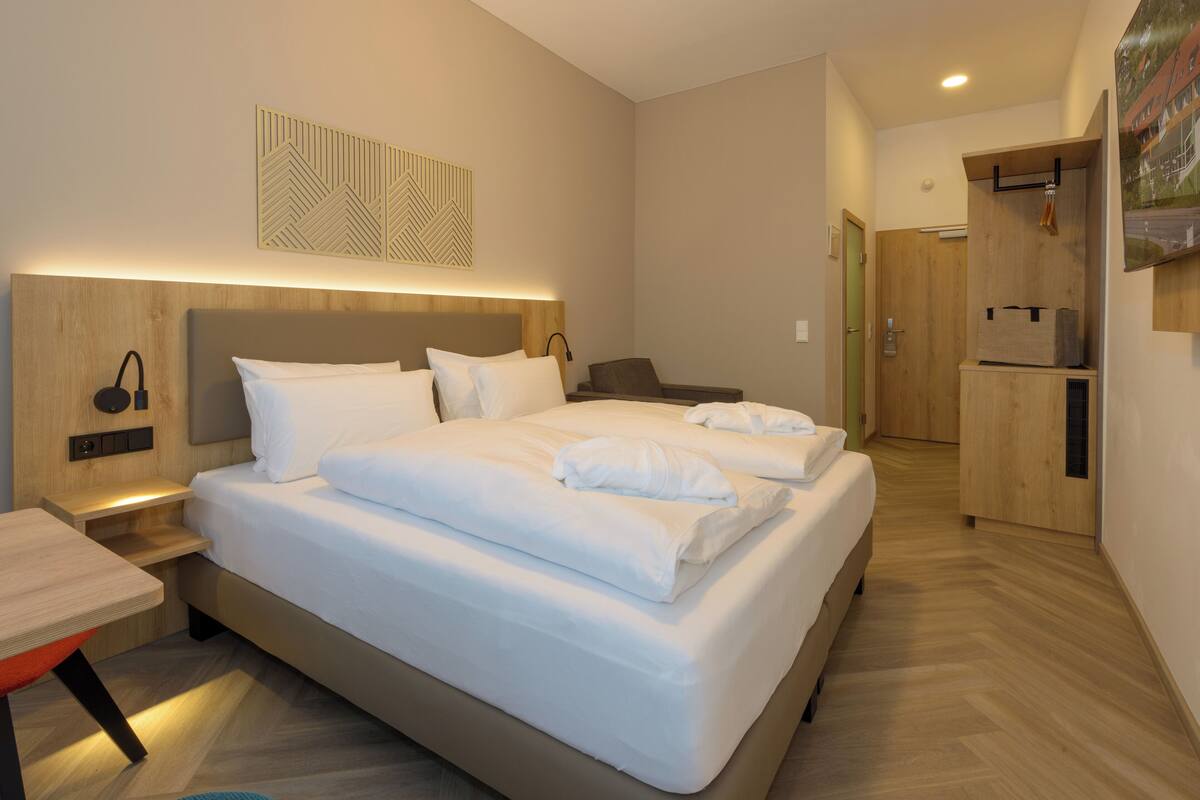 Ein modernes Hotelzimmer mit einem großen Bett, Nachttischen, einem Schreibtisch und einem Kleiderschrank.