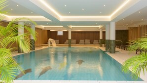 Une piscine intérieure offrant une vue dégagée sur l’ensemble de l’espace piscine, y compris le bord de la piscine, les chaises longues qui l’entourent et un coin salon avec vue sur la piscine.