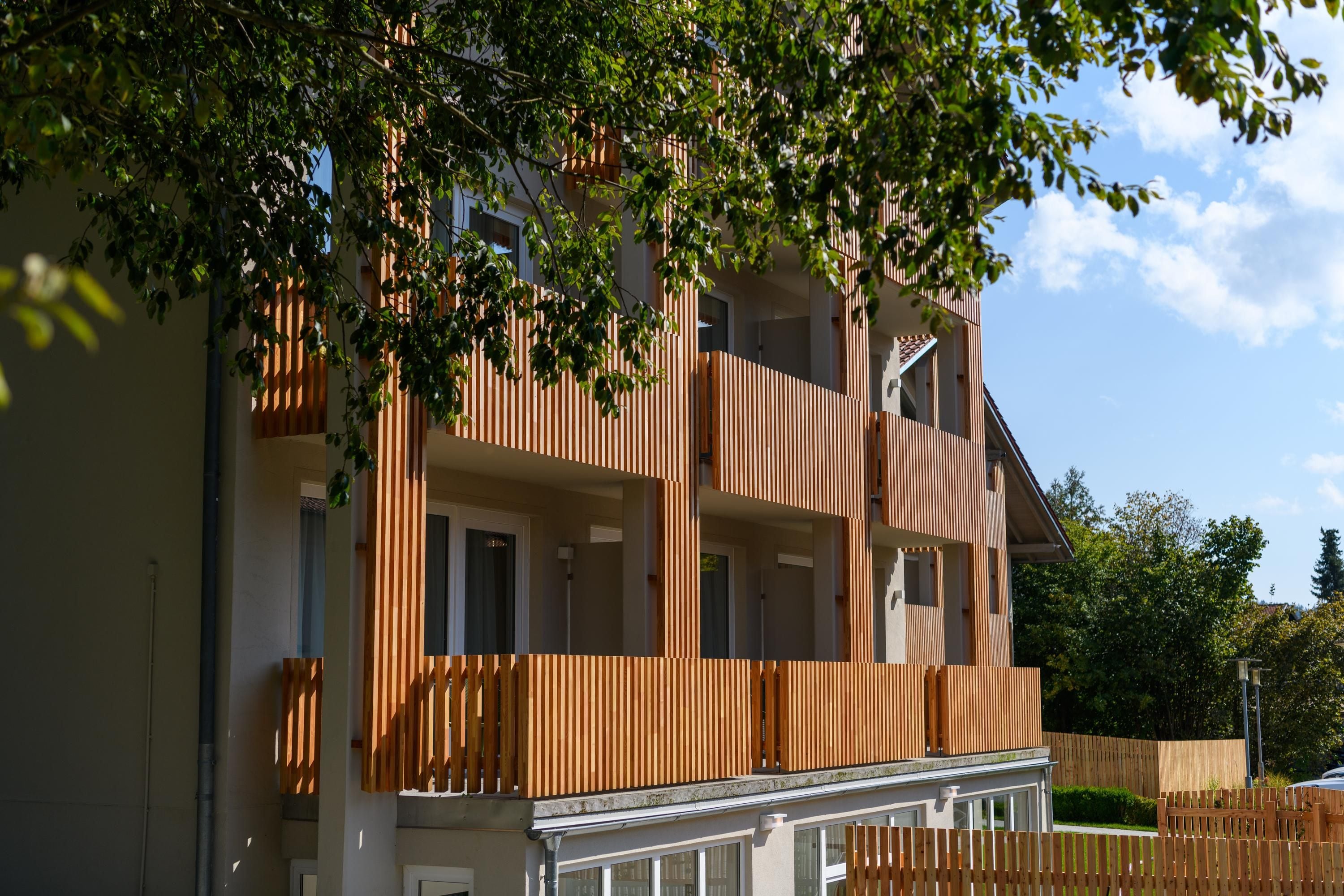 Un edificio residencial de varios pisos con un diseño moderno, que cuenta con balcones y fachada de madera.