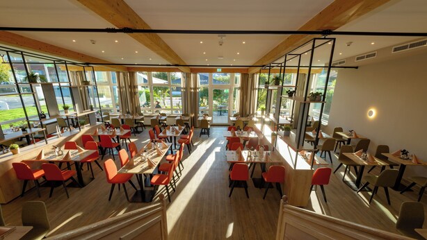 Un restaurant spacieux avec de hauts plafonds, de grandes fenêtres et un mélange de chaises rouges et brunes.