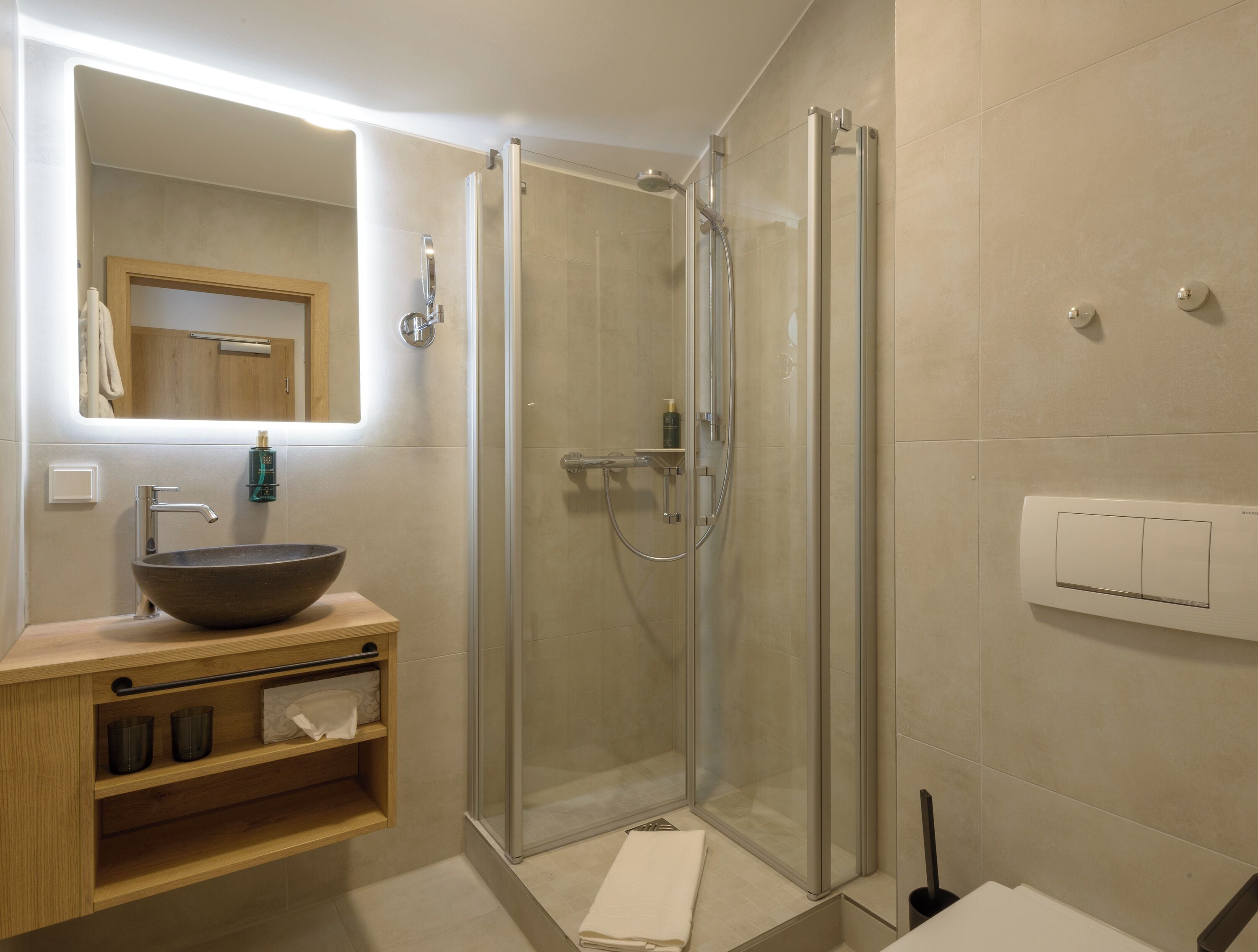 Un baño moderno con ducha de vidrio, tocador de madera con lavabo y un espejo sobre el lavabo.