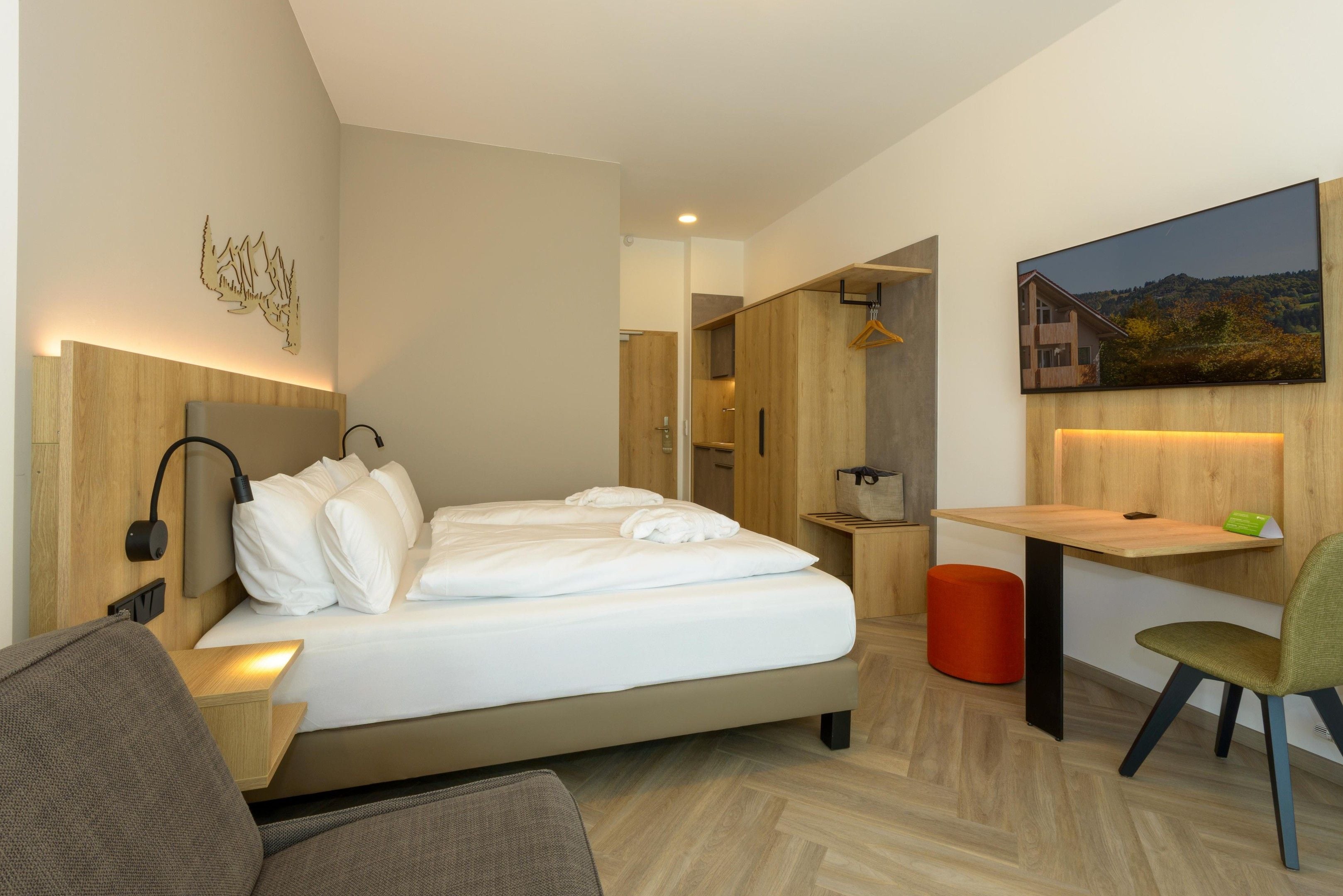 Ein modernes Hotelzimmer mit Bett, Nachttisch, Stuhl, Schreibtisch und einem Gemälde an der Wand.