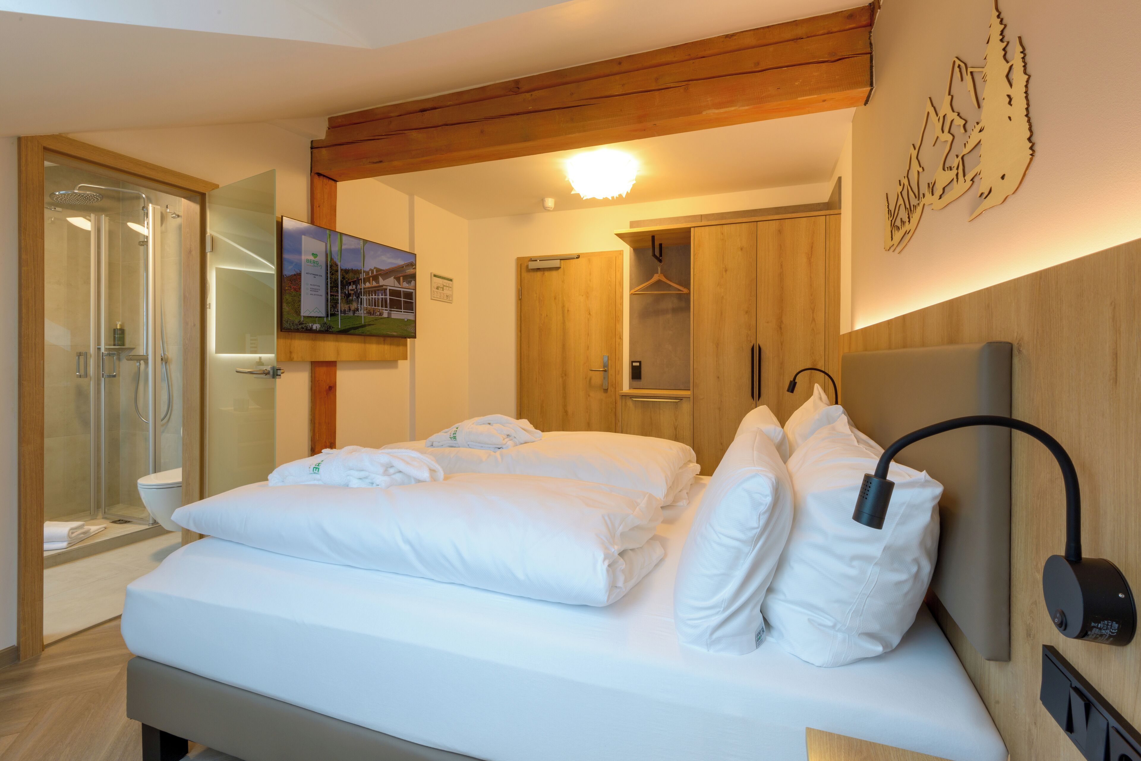 A hotel room with a bed, a shower, a wooden ceiling, and a wall-mounted TV.