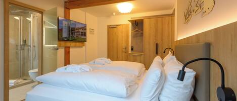 A hotel room with a bed, a shower, a wooden ceiling, and a wall-mounted TV.