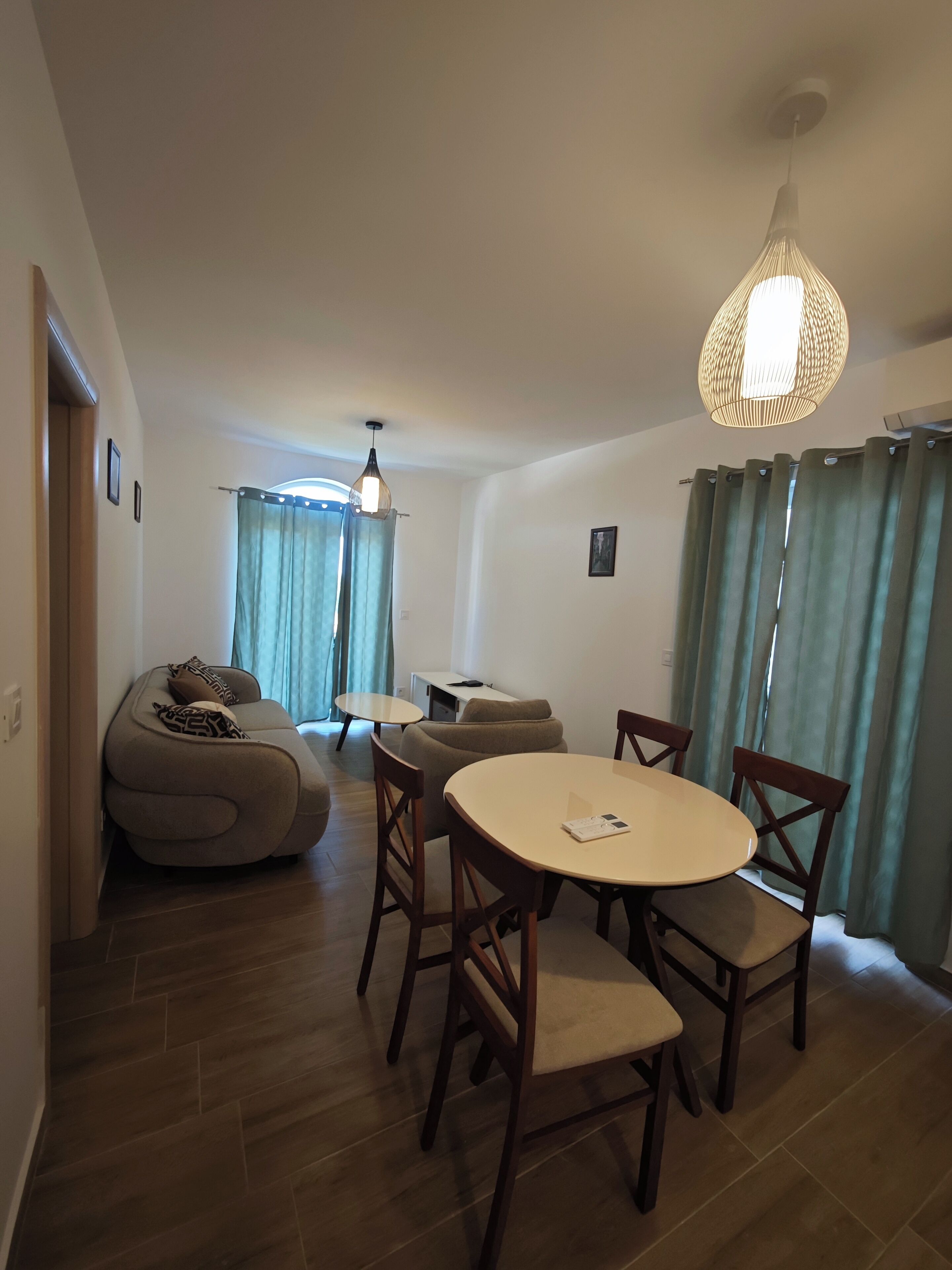 Ein modernes Wohnzimmer mit einem runden Esstisch, Holzstühlen, einer Couch und einer Hängeleuchte.