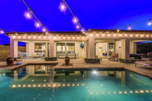 A modern pool house with a patio area, a pool, and string lights.