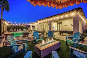 An outdoor pool area with lounge chairs, a fire pit, and string lights.